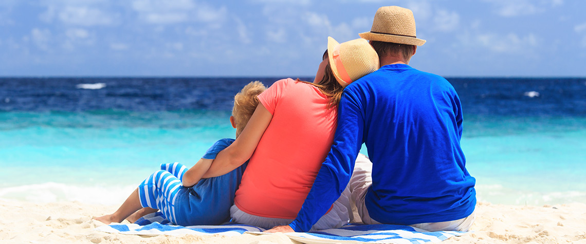 A view from behind a man, woman, and child at the beach on the shoreline