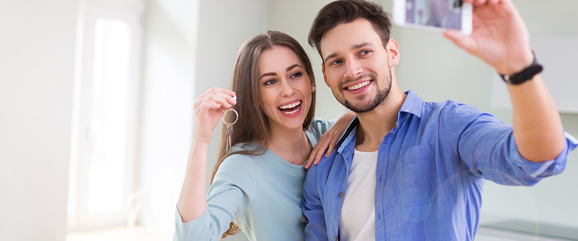 A male and female couple holding a home key while taking a selfie