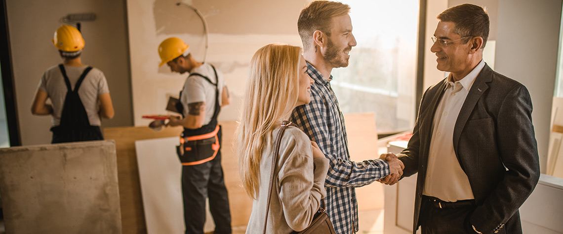 A male and female couple shaking hands with an architect on a job site