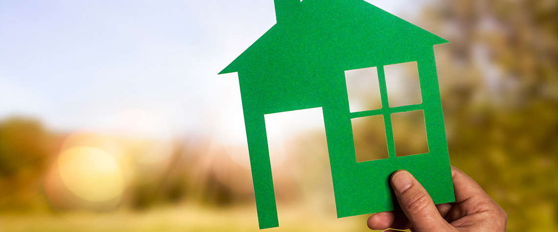 A paper cutout house being held up in front of an open field