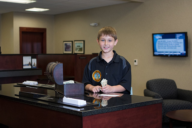 A boy holding money in front of a small treasure chest at the bank