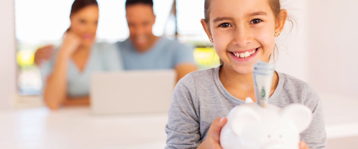 cheerful little girl holding piggybank with parents on background