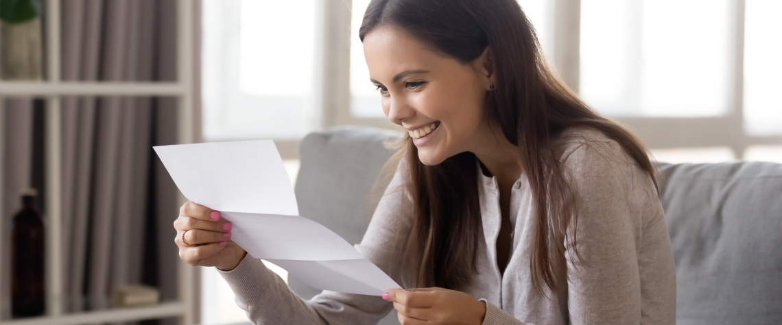 Excited young woman sitting on sofa reading college admission letter