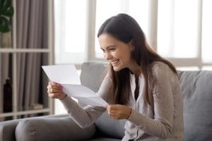 Excited young woman sitting on sofa reading college admission letter
