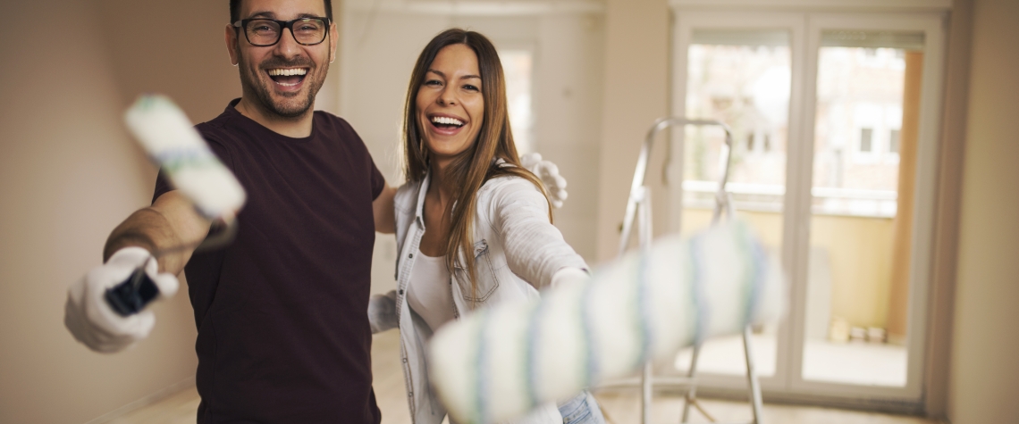 Smiling young couple in their apartment holding painting roller in their hands and laughing.