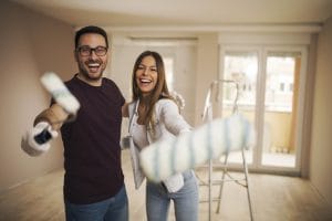 Smiling young couple in their apartment holding painting roller in their hands and laughing.