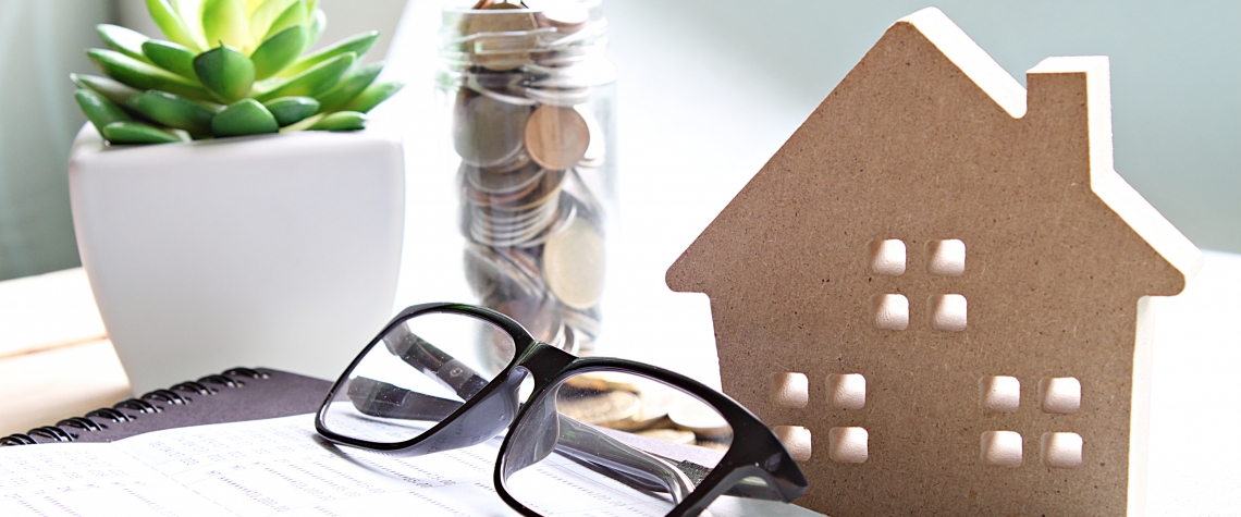 Wood house model, coins, eyeglasses and saving account book or financial statement on office desk table