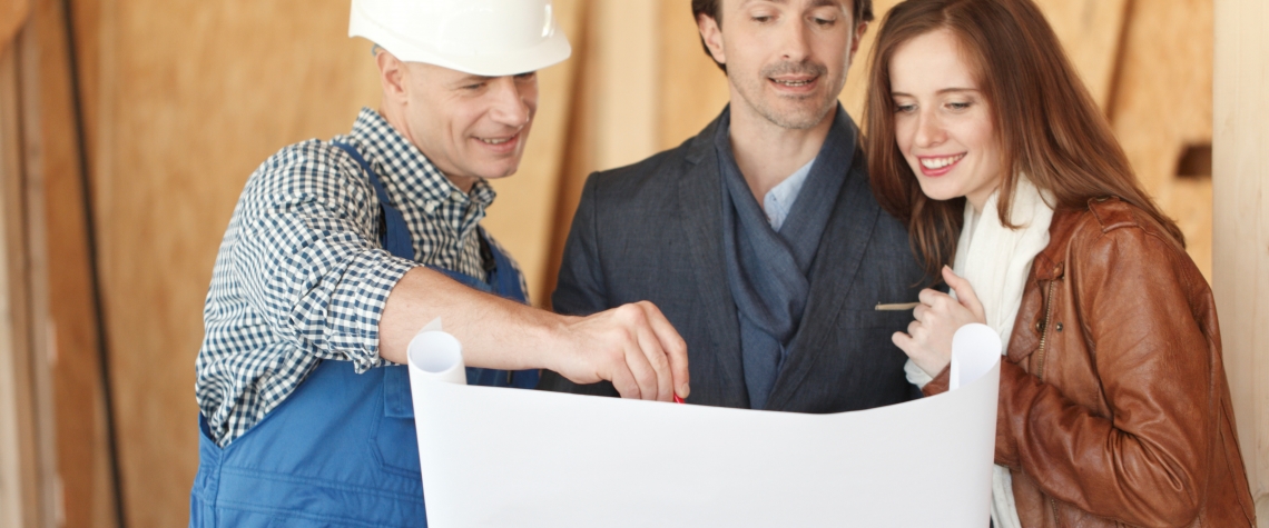 Worker shows house design plans to a young couple at construction site