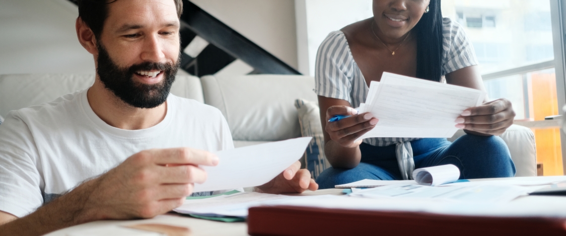 Multiethnic couple filing tax return. African American woman and Caucasian man checking utility bills and banking account. Front View.