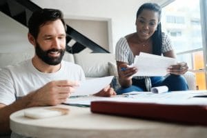 Multiethnic couple filing tax return. African American woman and Caucasian man checking utility bills and banking account. Front View.