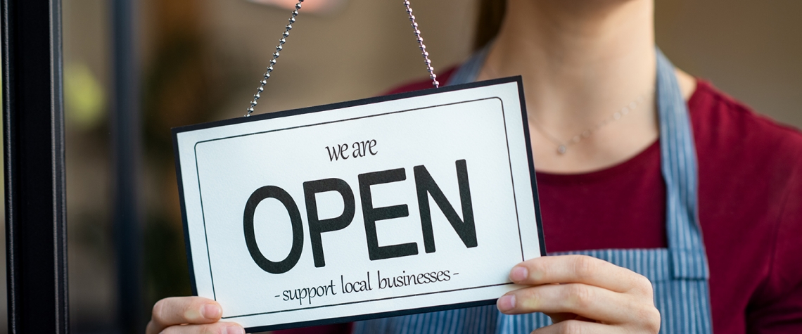 Small business owner smiling while turning the sign for the reopening of the place after the quarantine due to covid-19. Happy businesswoman standing at her restaurant or coffee shop gate with open signboard. Close up of woman