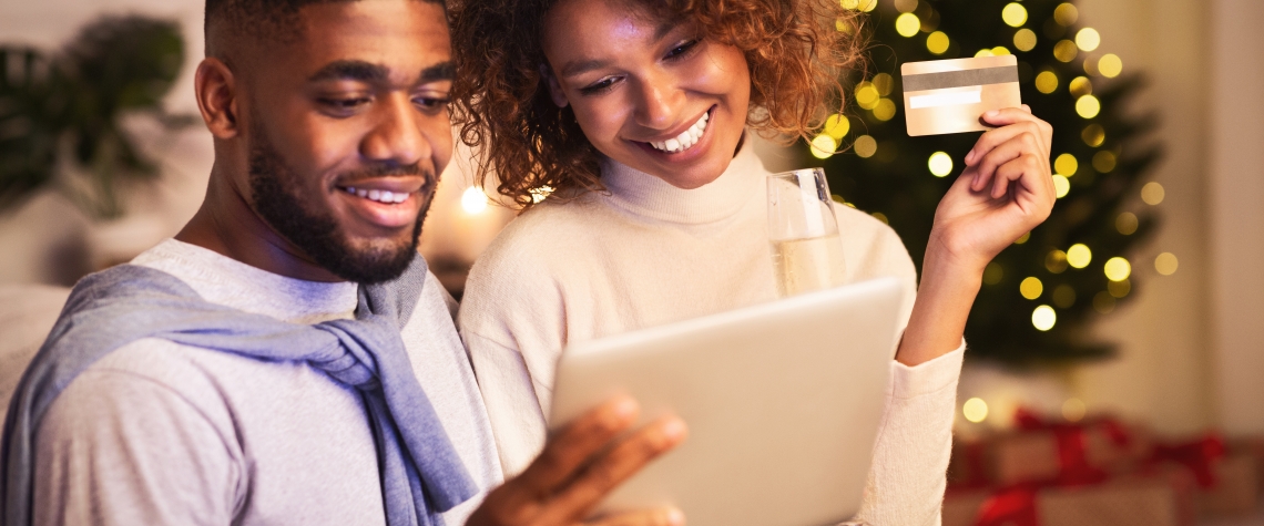 Christmas preparation. Happy black couple buying gifts online, using tablet and credit card