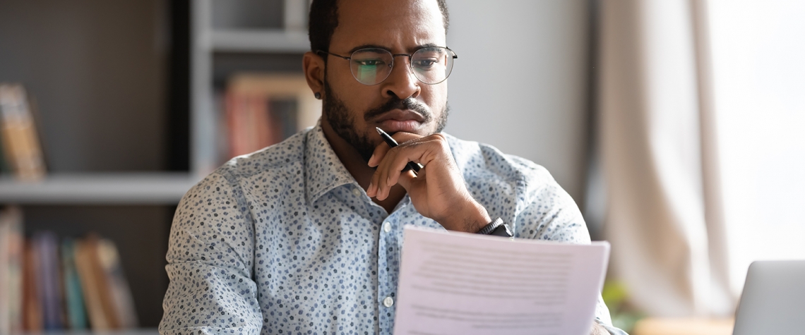 African student guy sit at desk hold papers tasks having difficulties with test, company lawyer read contract terms and detail feels discontented, received bad news from bank unpleasant letter concept