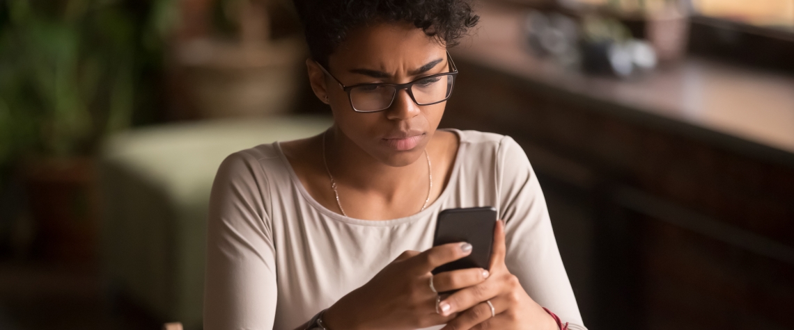 Upset confused african woman holding cellphone having problem with mobile phone, frustrated angry mixed race girl reading bad news in message looking at smartphone annoyed by spam or missed call