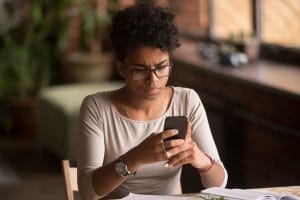 Upset confused african woman holding cellphone having problem with mobile phone, frustrated angry mixed race girl reading bad news in message looking at smartphone annoyed by spam or missed call
