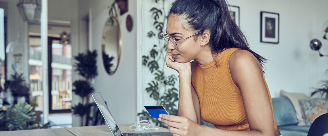 A woman is sitting at a dining table with a laptop and financial statements. Calculates and pays taxes and bills online.