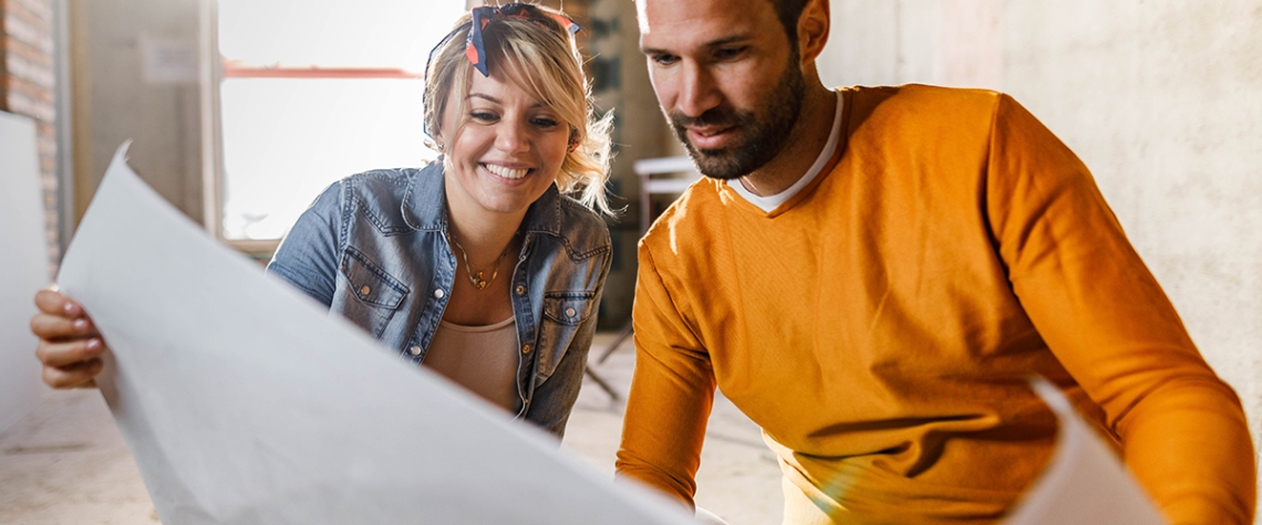 Young happy couple examining blueprints during home renovation process in the apartment. Focus is on woman.